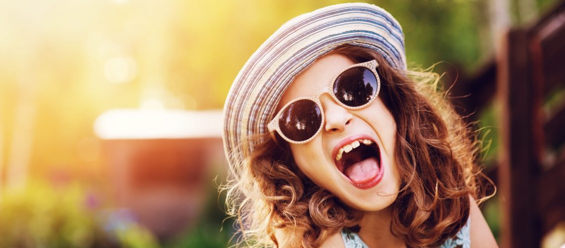 summer portrait of happy kid girl on vacation in sunglasses and hat, laugh and showing tongue.